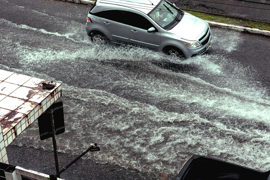 Car driving through flooded street during heavy rain.